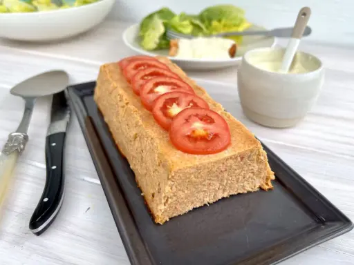 Un pain de thon savoureux, garni de rondelles de tomate fraîche, prêt à être dégusté avec une salade verte et une sauce crémeuse.