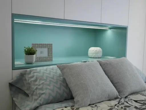 Habitación verde pistacho y gris con cama, almohadas y nicho iluminado.