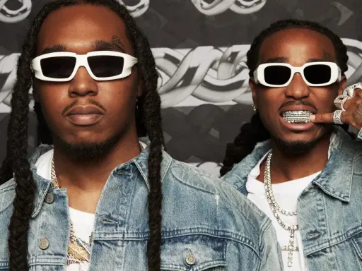 Två medlemmar av Migos, klädda i denimjackor och vita solglasögon, poserar med bling och grillz.