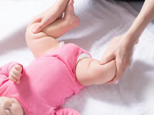 Delikatne badanie nóżek niemowlaka, uwaga skupiona na asymetrii fałdów udowych.