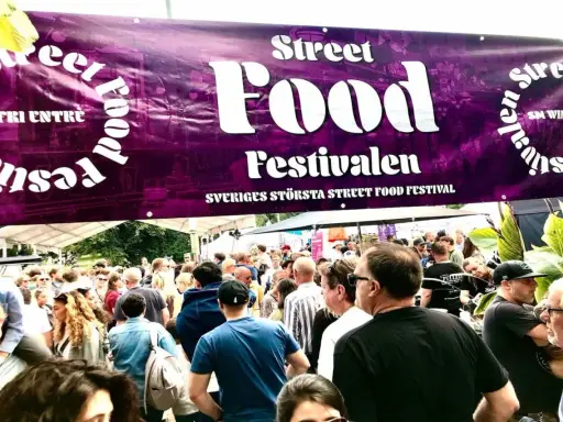 Stor folkmassa vid Sveriges största street food festival. En lila banderoll med texten "Street Food Festivalen" hänger över besökarna.