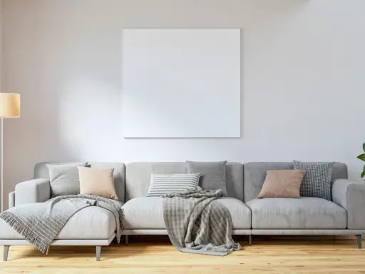 Sofá gris con cojines en tonos tierra y grises, mantas y planta. El color de cojines para sofá gris ideal para un ambiente acogedor.