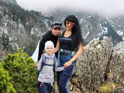 Rodzina na tle górskiej panoramy. Dziecko z flagą stoi na sarniej skale, obok rodzice.