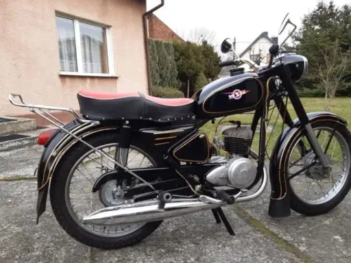 Czarny motocykl z PRL-u, z czerwonym siedzeniem i złotymi ozdobami. Klasyka polskich motocykli.