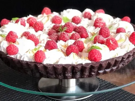 Pyszna tarta czekoladowa z malinami, udekorowana bitą śmietaną i listkami mięty. Idealna na deser.