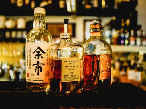 Tre flaskor japansk sprit, inklusive Nikka Whisky From The Barrel och Yoichi, står uppradade på en mörk yta.