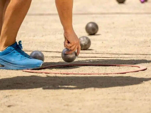 Une main saisit une boule de pétanque, prête à la lancer dans le cercle. Les règles du jeu de boules sont simples : viser le cochonnet.