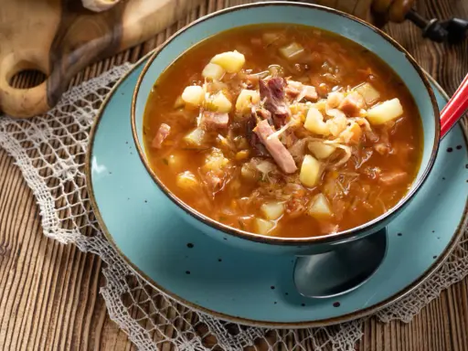 Aromaticzny kapuśniak jak u babci, pełen ziemniaków i wędzonki, w niebieskiej misce na drewnianym stole.