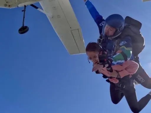 Ein Tandem-Fallschirmsprung – die perfekte Antwort auf die Frage, was schenkt man zum bestandenen Abitur. Zwei Menschen genießen den freien Fall vor strahlend blauem Himmel.