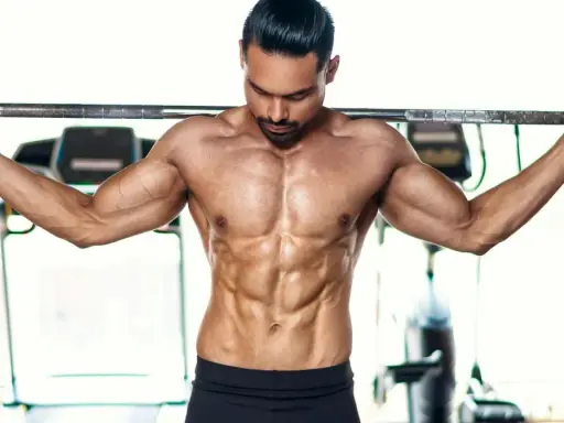 Ein Mann mit stark definierten Bauchmuskeln hält eine Langhantel im **cutten gym**.