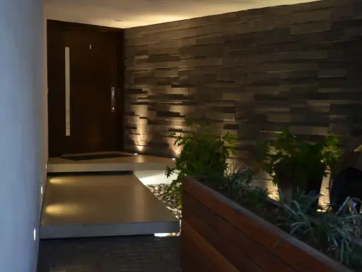 Ingresso con gradino interno illuminato, porta scura, muro in pietra e piante.