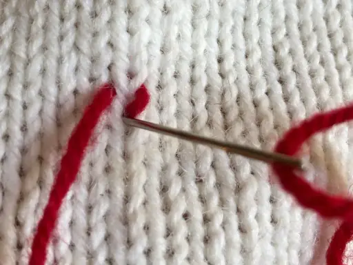 Nål med rött garn syr ihop stickat med maskstygn.