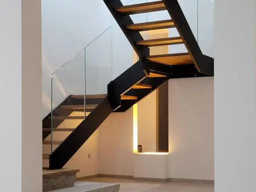 Scala interna con gradini in legno e struttura metallica nera. Il parapetto in vetro trasparente dona leggerezza al design moderno.