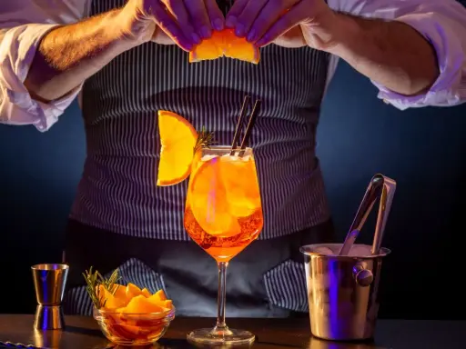 Barman prepara un Aperol Spritz, mostrando los distintos tipos de aperol y sus guarniciones.