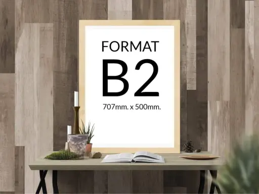 Ramka z napisem "FORMAT B2 707mm. x 500mm." na tle drewnianej ściany. Na stole obok świece, rośliny i otwarta książka.