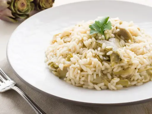 Un cremoso risotto con carciofi freschi, guarnito con un ciuffo di prezzemolo, pronto per essere gustato.