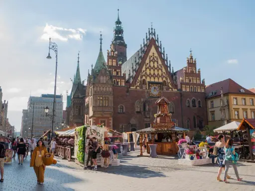 Wrocław stare miasto tętni życiem. Ludzie spacerują po Rynku, podziwiając zabytkowy ratusz i kolorowe kramy.