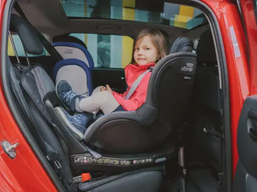Mała dziewczynka w czerwonej kurtce siedzi w foteliku samochodowym Britax Römer.
