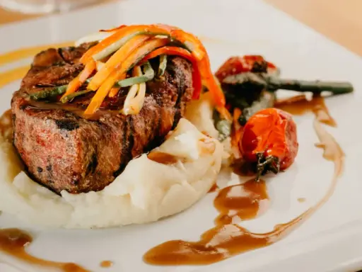 Un plat de viande grillée, purée de pommes de terre et légumes, une des spécialités d'Aurillac, servi sur une assiette blanche avec une sauce brune.