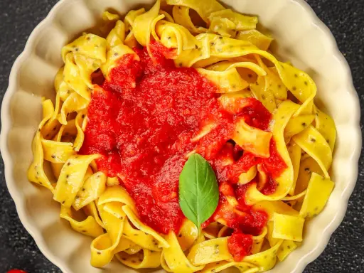 Pappardelle z sosem pomidorowym i bazylią, klasyczne makaron po włosku, podane w kremowej misce.