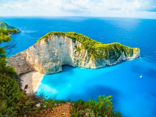 Widok na Navagio Beach, jedną z najpiękniejszych greckich atrakcji. Białe klify, turkusowa woda i zielona roślinność tworzą rajski krajobraz.