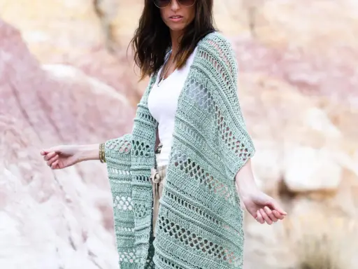 Mujer con gafas de sol luciendo un chaleco de **mantones de crochet** verde menta, con un diseño calado y mangas anchas, sobre una camiseta blanca y pantalones beige.