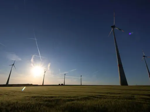 Windräder im Feld bei Sonnenuntergang, ein Symbol für den Windkraftausbau Deutschland. Kondensstreifen kreuzen den blauen Himmel.