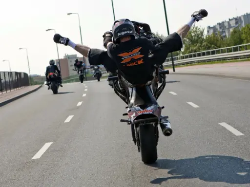 Motocyklista wykonuje jazdę na jednym kole z nogami w powietrzu. Ryzykowne wyczyny mogą skończyć się mandatem.