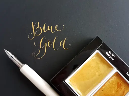 Złoty napis "Blue Gold" obok pióra i palety farb.