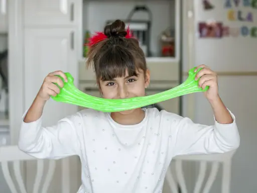 Bambina sorridente con slime verde brillante, un divertente esperimento per la ricetta slime fatta in casa.