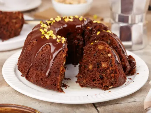 Pyszna babka na oleju, polana czekoladą i posypana pistacjami, z kawałkiem na talerzyku.