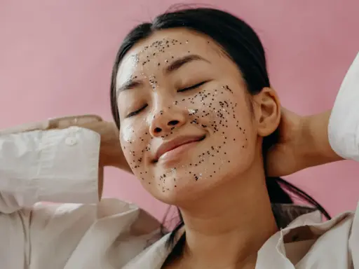 Une jeune femme au visage couvert d'un masque exfoliant scintillant, profitant d'un moment de détente. Elle nous rappelle pourquoi exfolier sa peau est essentiel pour un teint éclatant.