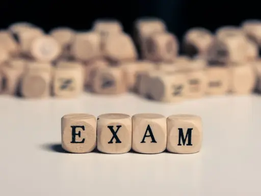 Drewniane kostki z literami tworzą napis "EXAM". Zastanawiasz się, na jakim poziomie jest matura podstawowa z angielskiego?