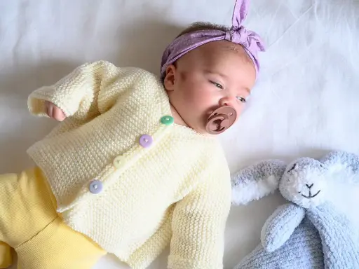 Un bebé con un suéter tejido a dos agujas y un conejito de peluche. El suéter es un muestrario de puntos a dos agujas para bebes.