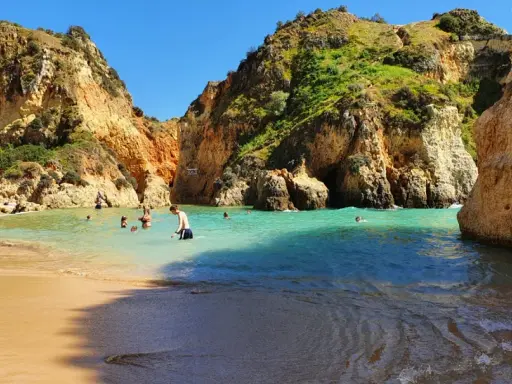 Sonnige Bucht mit Felsen und türkisfarbenem Wasser. Menschen baden und genießen das milde Wetter im **Portugal im Dezember**.