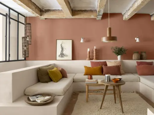 Salon cosy aux murs couleur brun terre de France, banquette en L, coussins ocre et rouille, table basse en bois brut.