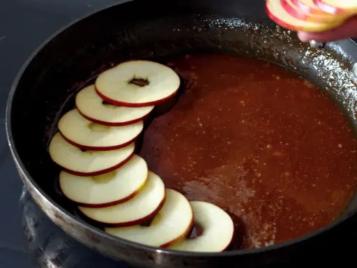 Äppelringar läggs i en panna med karamelliserad sås, förberedelse för en klassisk tarte tatin.