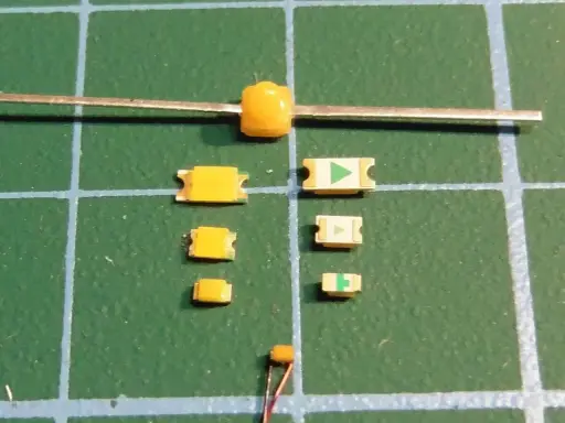 Mehrere kleine gelbe LEDs liegen auf einer grünen Schneidematte. Eine größere gelbe LED ist an einem Metallstift befestigt.