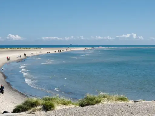 En vacker strandpromenad vid Skagen, med folk som njuter av solen och havet. En perfekt resa till Skagen.