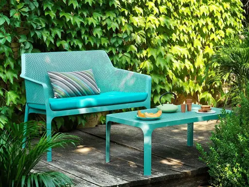 Divano e tavolino Nardi Spa Chiampo in un giardino rigoglioso, con cuscini color acqua e un set da tè.
