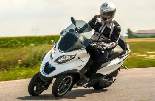 Biały Piaggio MP3 500 z kierowcą w kasku pędzi po drodze. Zastanawiasz się nad jego spalaniem?
