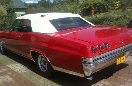 Czerwona kabrioletowa Chevy Impala z białym dachem, zaparkowana na podjeździe z kostki brukowej.