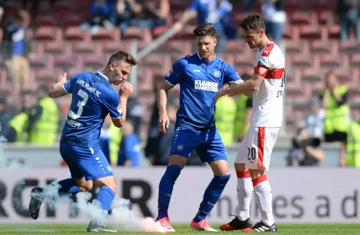 Piłkarze Karlsruher SC w niebieskich strojach, jeden z nich z numerem 3, otoczeni dymem z rac.