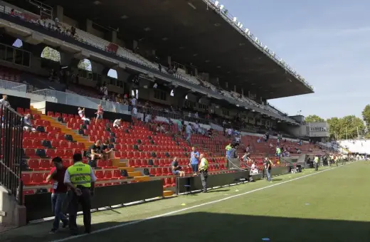 Puste trybuny stadionu Vallecas, z kilkoma osobami siedzącymi i stojącymi.