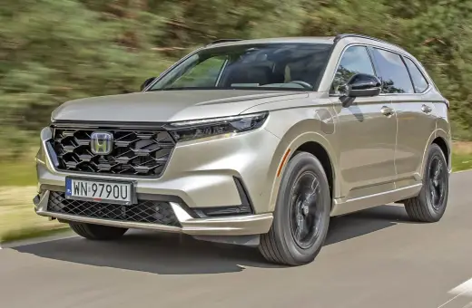 Nowy Honda CR-V w kolorze złotym jedzie po drodze, otoczony zielenią.