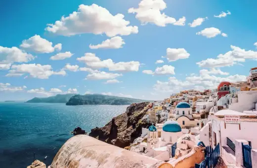 Widok na białe domy z niebieskimi kopułami na Santorini. Zastanawiasz się, ile się leci do Grecji, by podziwiać takie krajobrazy?