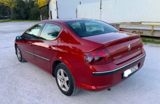 Błyszczący czerwony Peugeot 407 2.0 HDI z przyciemnianymi szybami stoi na żwirowym podjeździe.
