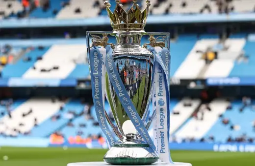 Trofeum za mistrzostwo Anglii, błyszczące i ozdobione wstążkami Premier League, stoi na tle stadionu.