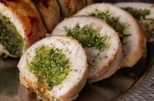 Pokrojona rolada z indyka faszerowana zielonym farszem, podana na metalowej tacy.