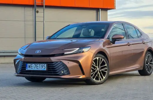 Brązowa Toyota Camry 2.5 Hybrid z eleganckimi felgami stoi na tle nowoczesnego budynku.